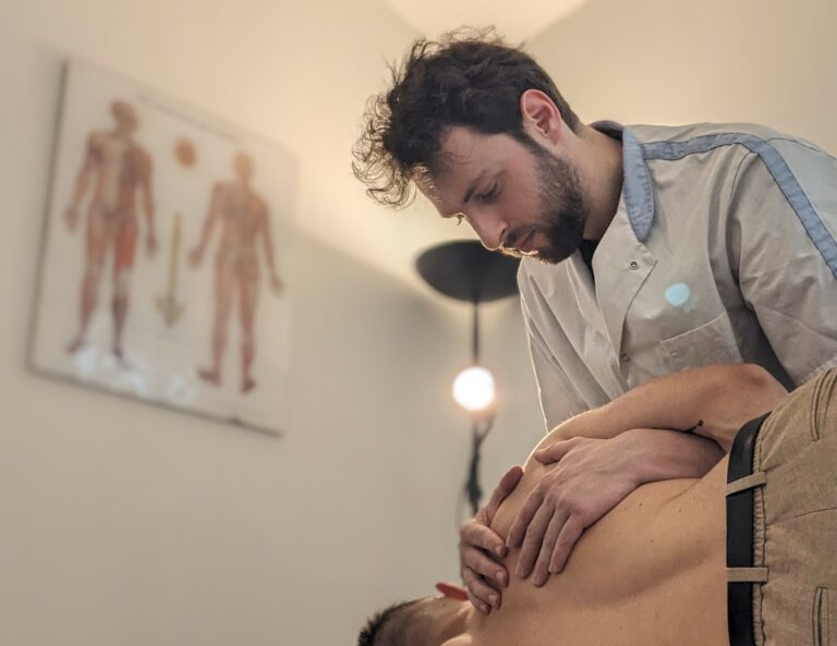 2 hommes, un est allongé sur le côté, l'autre a les mains sur son omoplate et est penché vers lui, en fond, un lampadaire et deux planches d'anatomie